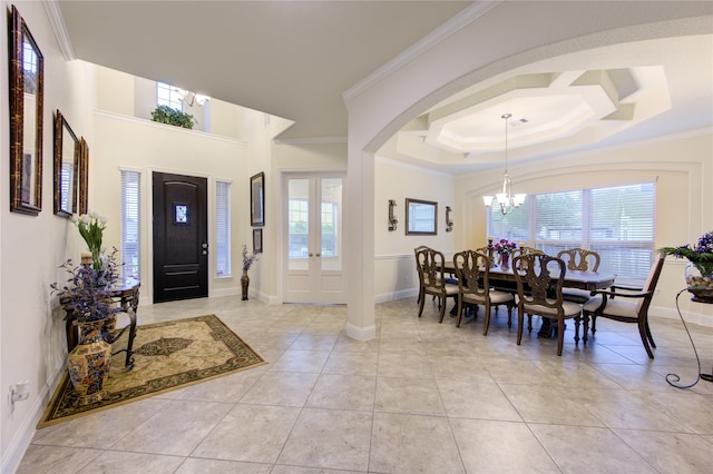 tiled foyer featuring french doors, a notable chandelier, a raised ceiling, and ornamental molding