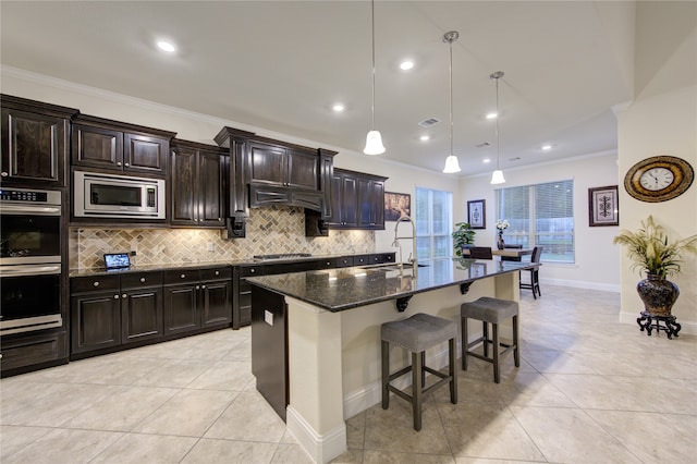 kitchen with appliances with stainless steel finishes, ornamental molding, a kitchen breakfast bar, decorative light fixtures, and a kitchen island with sink