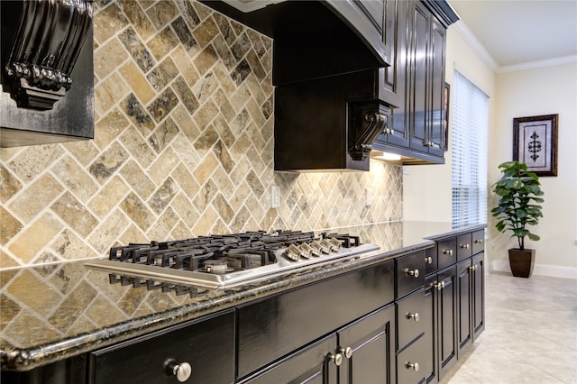 kitchen featuring ornamental molding, dark brown cabinetry, decorative backsplash, stainless steel gas stovetop, and dark stone countertops