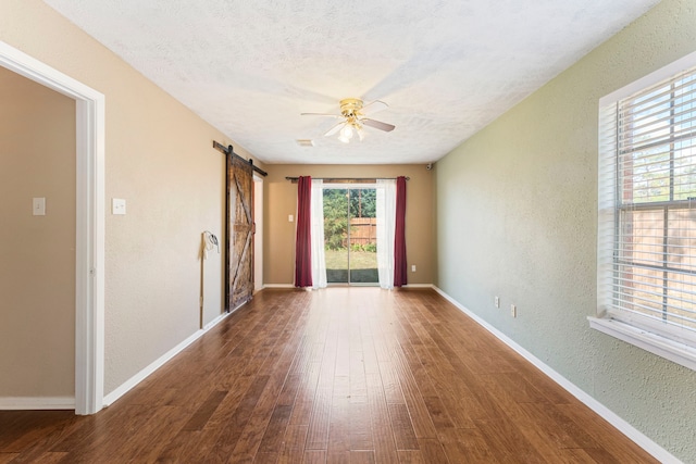 empty room with a textured ceiling, a barn door, hardwood / wood-style flooring, and ceiling fan