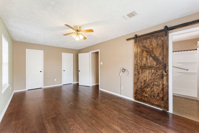 unfurnished bedroom with dark wood-type flooring, ceiling fan, a textured ceiling, and a barn door