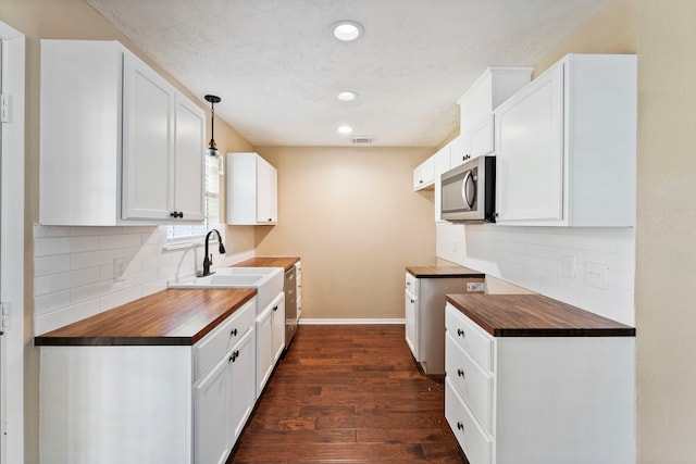 kitchen featuring sink, butcher block countertops, white cabinetry, pendant lighting, and dark hardwood / wood-style floors