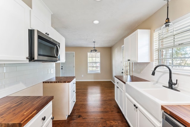 kitchen with white cabinets, hanging light fixtures, dark hardwood / wood-style flooring, butcher block counters, and stainless steel appliances