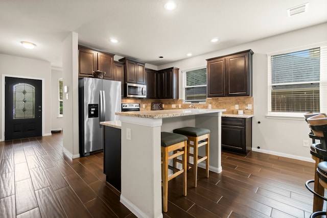 kitchen featuring tasteful backsplash, dark brown cabinets, a kitchen island, and appliances with stainless steel finishes