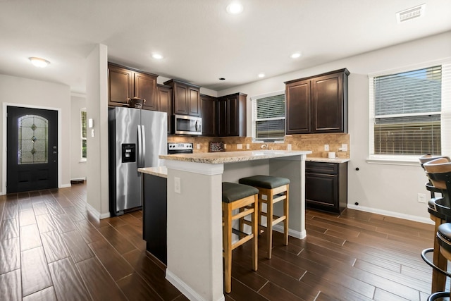 kitchen featuring stainless steel appliances, a kitchen island, backsplash, and dark brown cabinetry