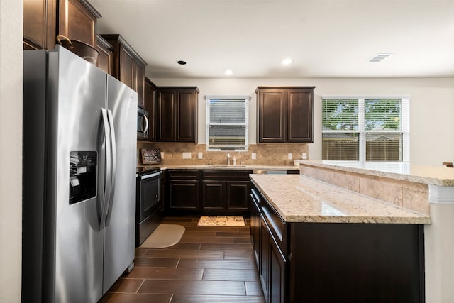 kitchen featuring light stone countertops, appliances with stainless steel finishes, backsplash, sink, and a center island