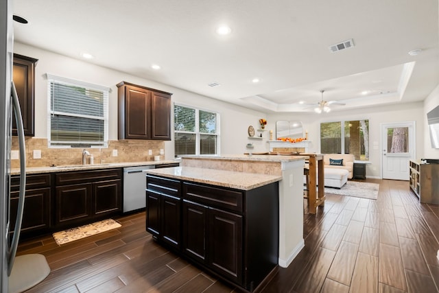 kitchen featuring a raised ceiling, sink, appliances with stainless steel finishes, dark brown cabinets, and a kitchen island