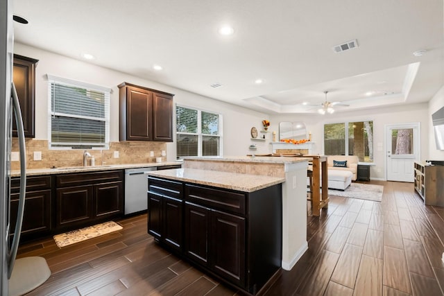 kitchen with sink, a tray ceiling, dishwasher, a kitchen island, and backsplash