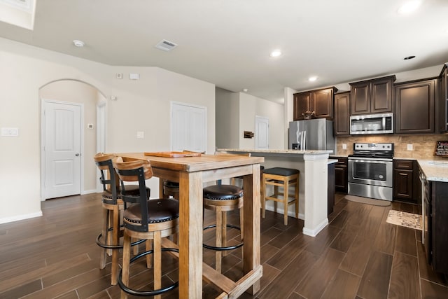 kitchen with light stone countertops, stainless steel appliances, backsplash, a kitchen bar, and a kitchen island