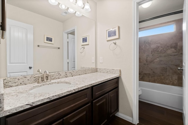 full bathroom with hardwood / wood-style flooring, tiled shower / bath, vanity, and toilet