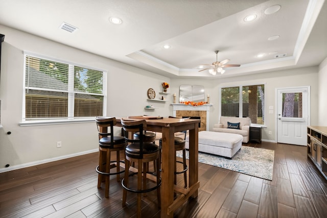 dining room featuring a tile fireplace, a raised ceiling, dark wood-type flooring, and crown molding