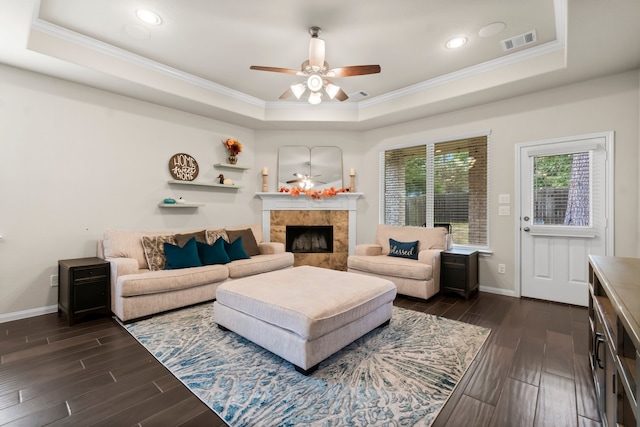 living room featuring a tray ceiling, a tiled fireplace, and crown molding