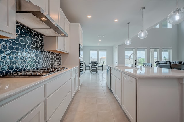 kitchen featuring wall chimney range hood, pendant lighting, sink, an island with sink, and white cabinets