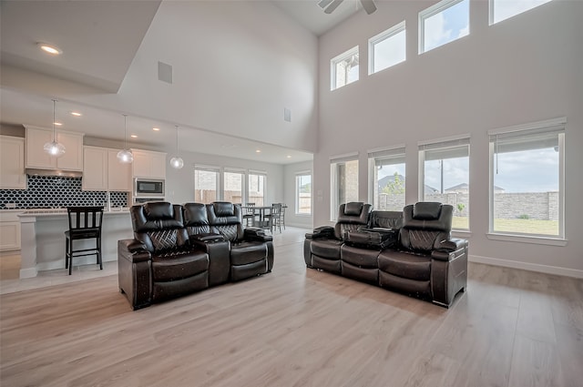 living room with a towering ceiling, ceiling fan, and light wood-type flooring