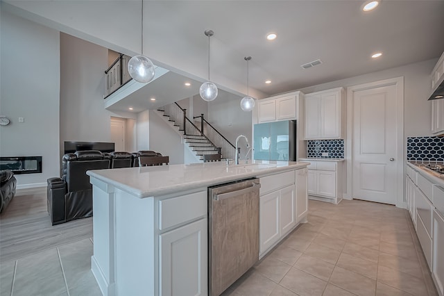 kitchen featuring stainless steel dishwasher, sink, an island with sink, and white cabinets