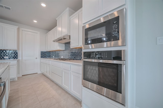 kitchen with stainless steel appliances, white cabinets, light tile patterned floors, and backsplash