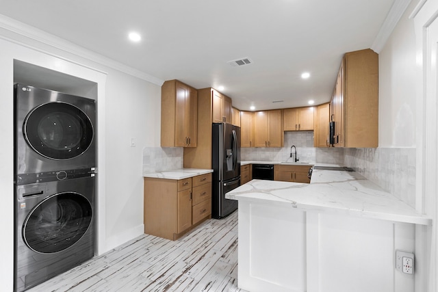 kitchen featuring sink, kitchen peninsula, stacked washing maching and dryer, ornamental molding, and stainless steel fridge with ice dispenser