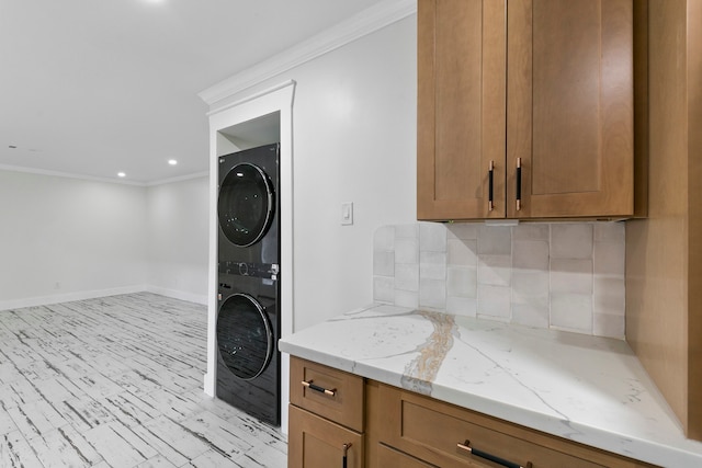 laundry room featuring crown molding and stacked washer and clothes dryer