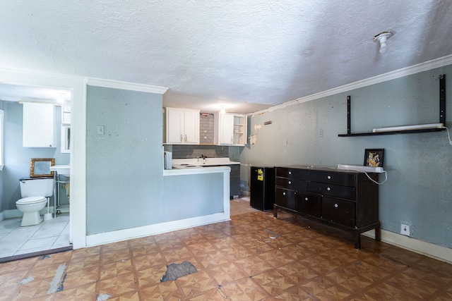 kitchen with crown molding, white cabinetry, a textured ceiling, and backsplash