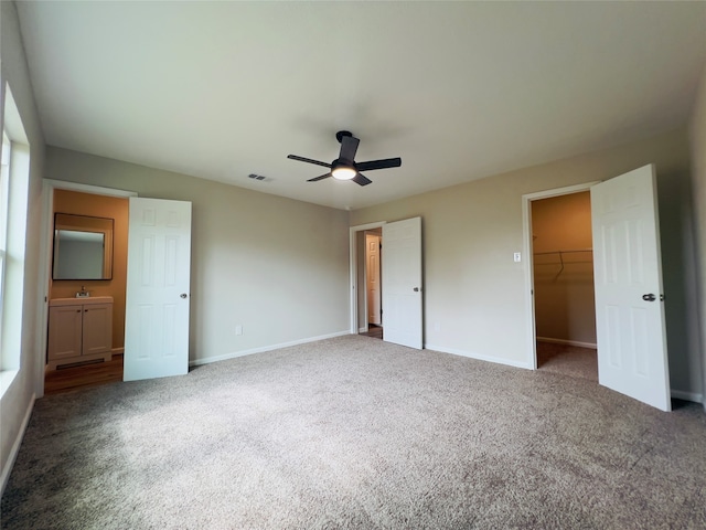 unfurnished bedroom with connected bathroom, a closet, a spacious closet, carpet, and ceiling fan