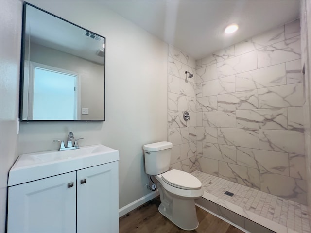 bathroom featuring vanity, a tile shower, wood-type flooring, and toilet