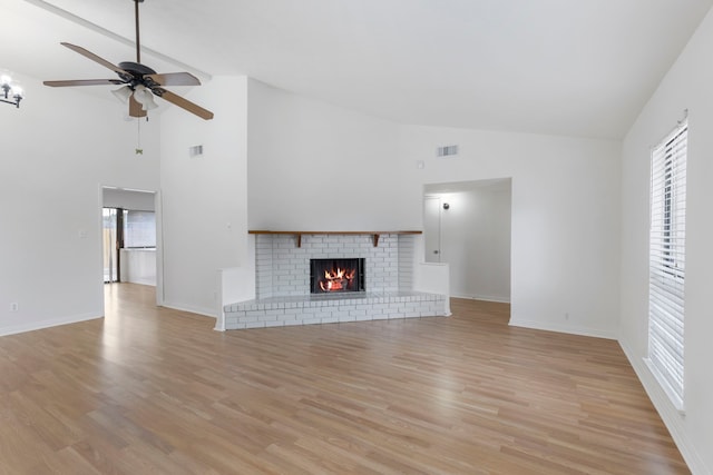 unfurnished living room with ceiling fan, high vaulted ceiling, a brick fireplace, and light wood-type flooring