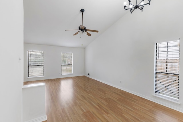 unfurnished living room with high vaulted ceiling, plenty of natural light, ceiling fan with notable chandelier, and light wood-type flooring