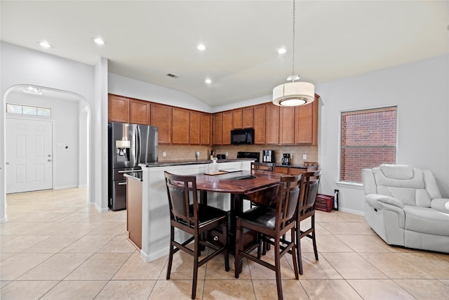 kitchen with lofted ceiling, decorative backsplash, an island with sink, stainless steel fridge with ice dispenser, and decorative light fixtures