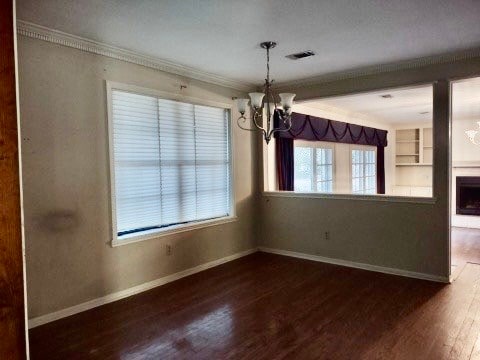 unfurnished dining area featuring ornamental molding, a notable chandelier, dark hardwood / wood-style floors, and built in features