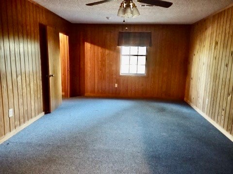 unfurnished room featuring wood walls, carpet floors, and ceiling fan