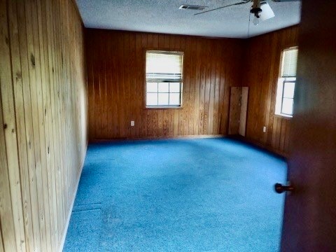 carpeted empty room with wood walls, plenty of natural light, and ceiling fan