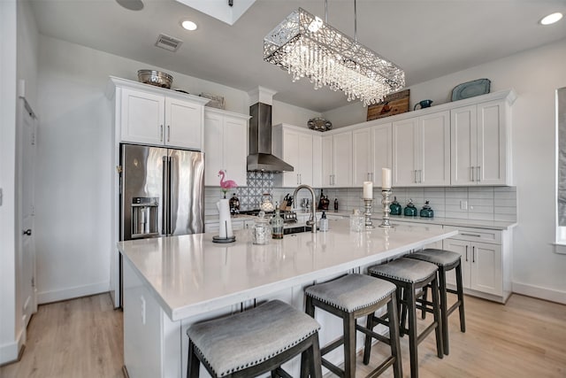 kitchen featuring a breakfast bar area, white cabinets, and wall chimney range hood