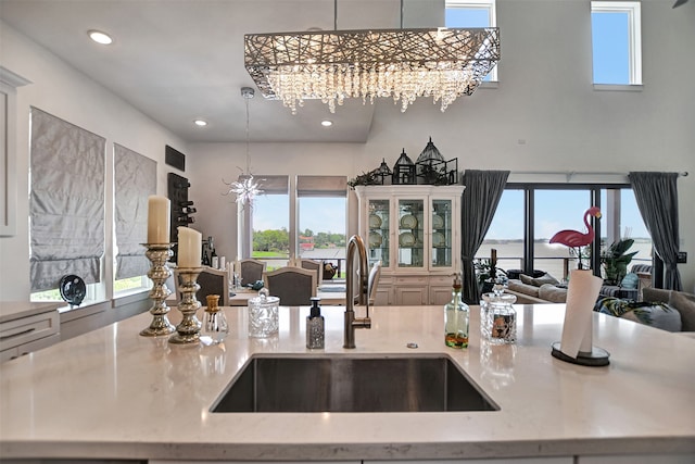 kitchen with sink, decorative light fixtures, an inviting chandelier, light stone counters, and a water view