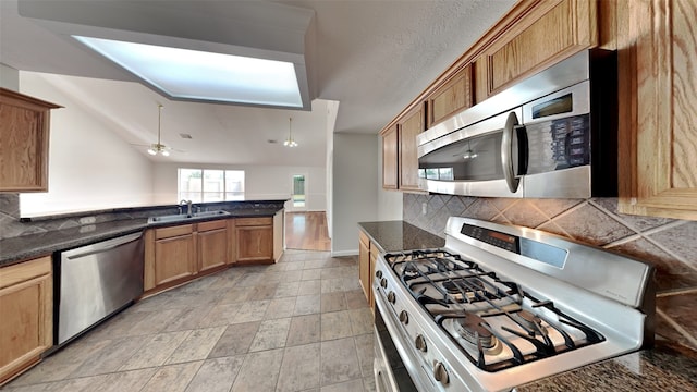 kitchen with lofted ceiling, backsplash, dark stone countertops, sink, and stainless steel appliances