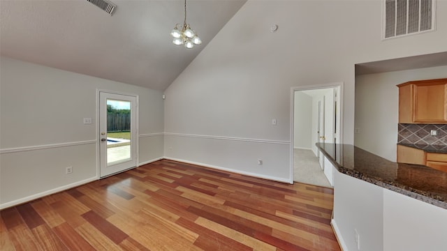 unfurnished dining area featuring light hardwood / wood-style floors, high vaulted ceiling, and an inviting chandelier