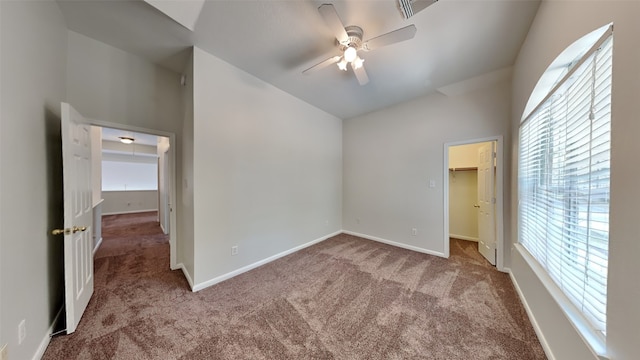 unfurnished bedroom with a walk in closet, light colored carpet, a closet, and ceiling fan