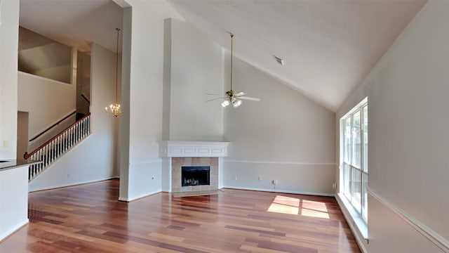 unfurnished living room featuring hardwood / wood-style floors, high vaulted ceiling, a tile fireplace, and ceiling fan with notable chandelier