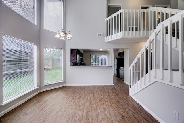 unfurnished living room with an inviting chandelier, hardwood / wood-style flooring, a towering ceiling, and plenty of natural light