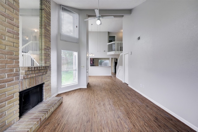 unfurnished living room with a towering ceiling, wood-type flooring, a fireplace, ceiling fan, and beam ceiling