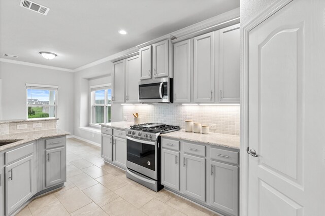 kitchen with tasteful backsplash, light stone countertops, gray cabinets, crown molding, and stainless steel appliances