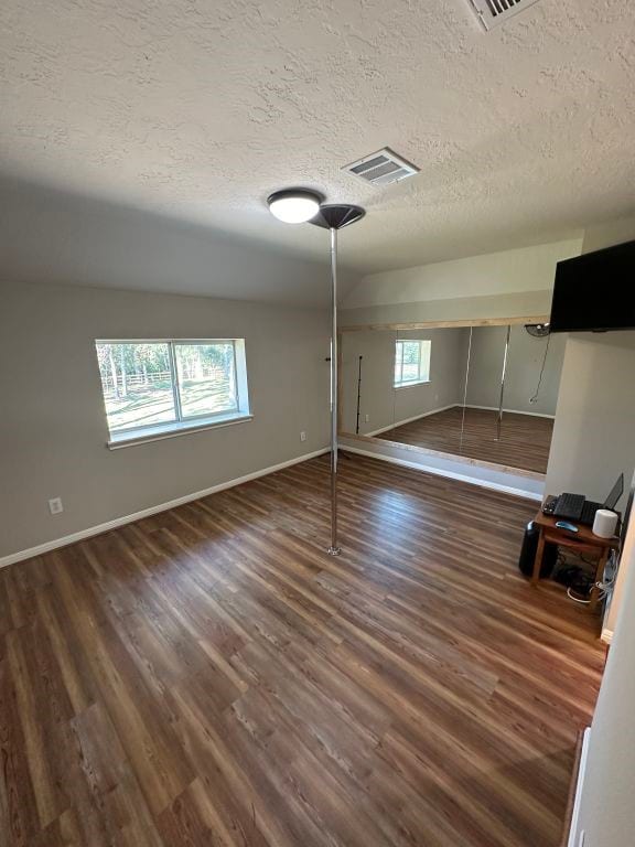 basement with a wealth of natural light, dark wood-type flooring, and a textured ceiling