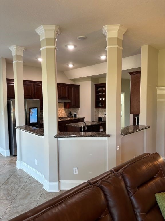 kitchen with kitchen peninsula, dark stone counters, dark brown cabinetry, tasteful backsplash, and stainless steel refrigerator