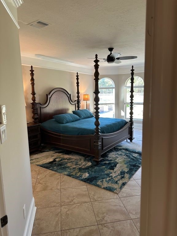 tiled bedroom with ornamental molding, a textured ceiling, and ceiling fan