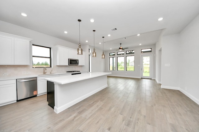 kitchen featuring a kitchen island, a ceiling fan, appliances with stainless steel finishes, a sink, and light countertops