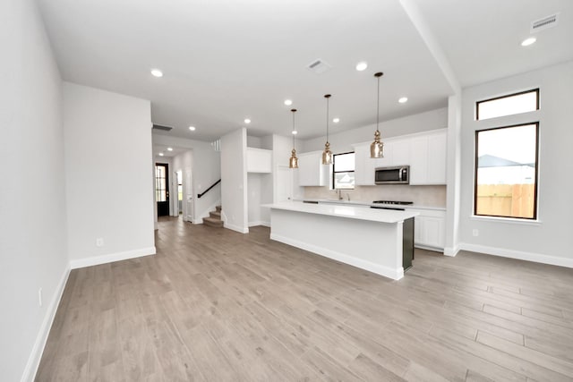 kitchen featuring visible vents, a kitchen island, light countertops, stainless steel microwave, and white cabinets