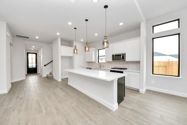 kitchen with a center island, light countertops, white cabinetry, stainless steel microwave, and a sink