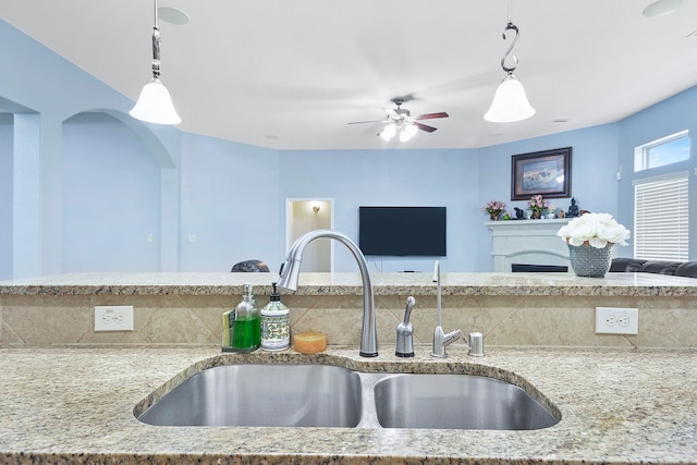 kitchen with light stone counters, sink, hanging light fixtures, and ceiling fan