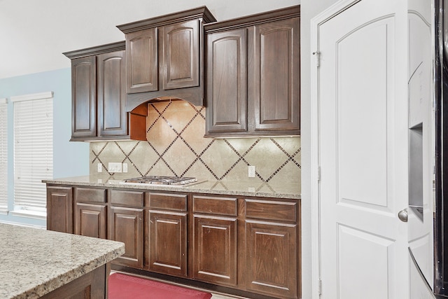 kitchen with stainless steel gas stovetop, light stone countertops, dark brown cabinets, and backsplash