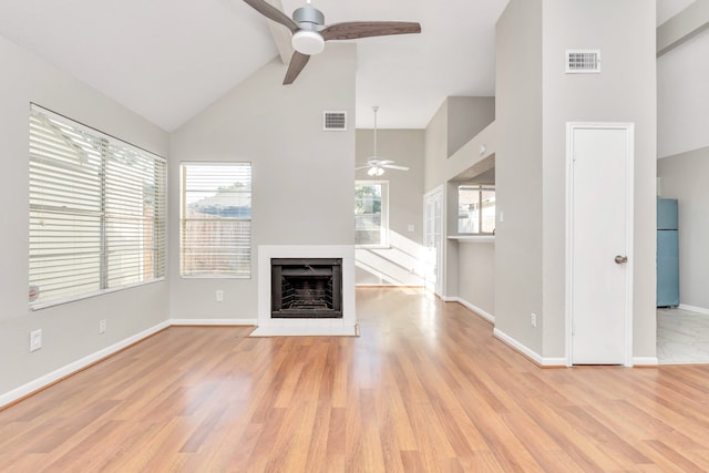 unfurnished living room with high vaulted ceiling, light wood-type flooring, and plenty of natural light