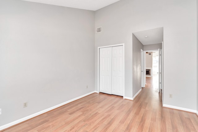 unfurnished bedroom with a closet, a high ceiling, and light wood-type flooring